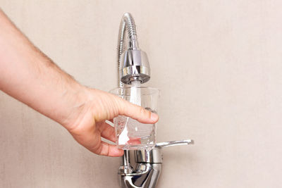 The hand of a man with a glass pouring water from a tap with a copy space