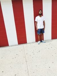 Full length portrait of young man standing against red wall