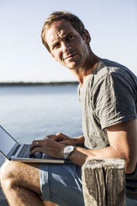 Mature man looking away while using laptop on pier