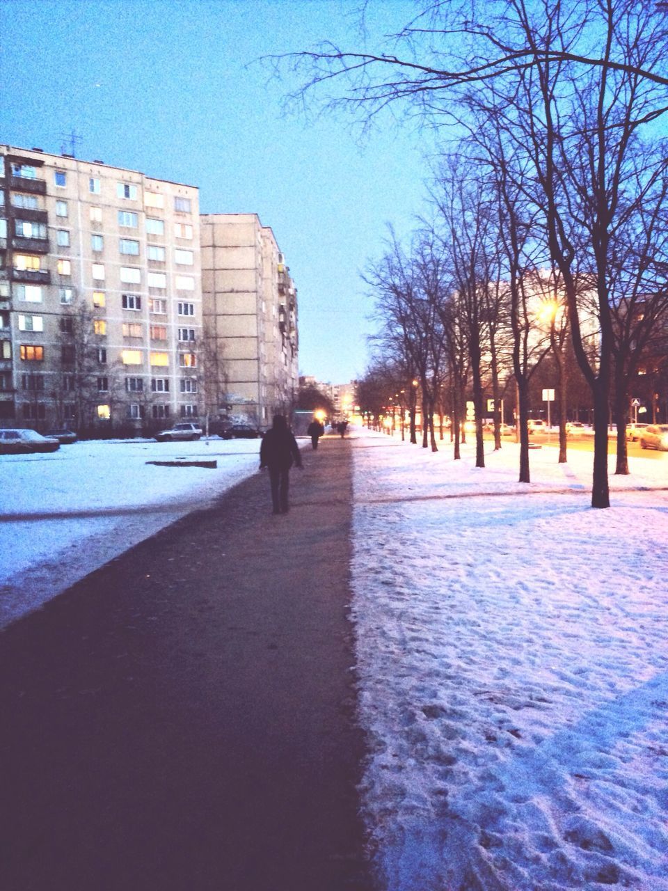 SNOW COVERED ROAD BY BUILDINGS AGAINST SKY