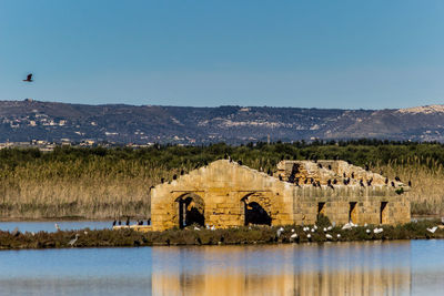 Built structure by lake against clear blue sky