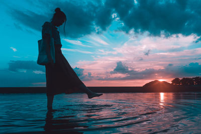Silhouette woman standing by sea against sky during sunset