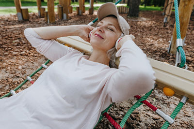 Mature woman listening to music and relaxing on hammock in park