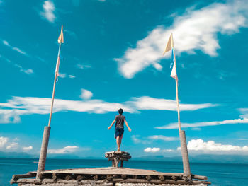 Rear view of man standing at pier against sky