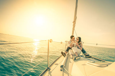 Romantic couple sitting on boat in sea against clear sky during sunset