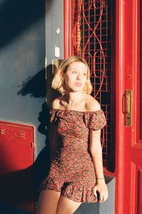 Portrait of beautiful young woman standing against door