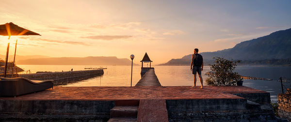 Man standing by sea against sky during sunset