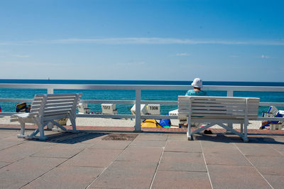 Rear view of chairs on beach against blue sky