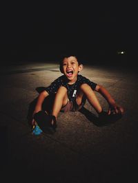 Cute boy shouting while sitting on footpath in city at night