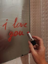 Close-up of hand writing on wall with lipstick