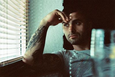 Portrait of young man looking through window at home