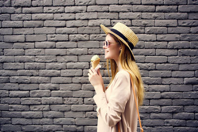 Portrait of woman holding ice cream against brick wall
