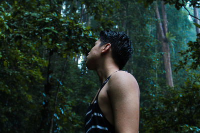 Side view of young man standing in forest during rainy season
