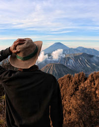 Rear view of man holding hat against mountains