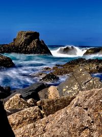 Scenic view of rocks in sea against clear blue sky