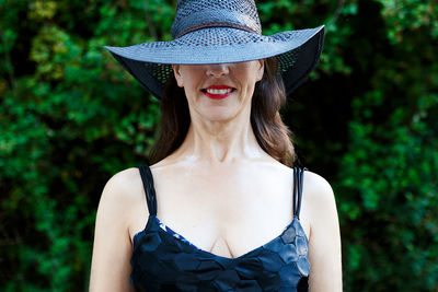 Smiling woman wearing hat standing against plants