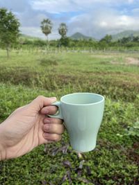 Hand holding tea cup on field