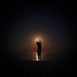 Silhouette man standing on beach against sky at night