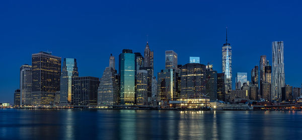 Buildings at waterfront against blue sky at night