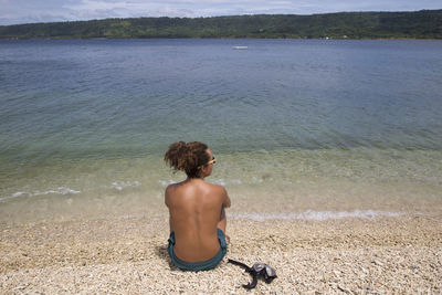 Rear view of shirtless man looking at sea