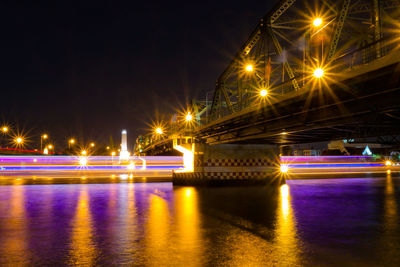 Illuminated bridge over river against sky at night