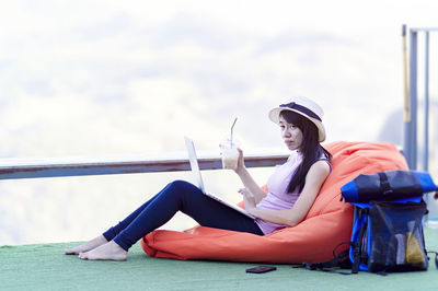 Young woman sitting on chair against sky