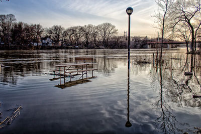 Reflection of bare trees in lake against sky