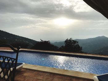 Swimming pool by lake against sky during sunset