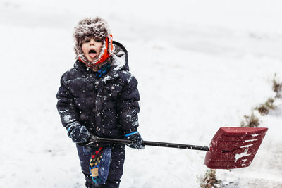 Portrait of boy holding shovel while standing on snow covered field