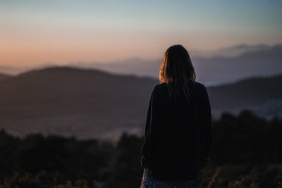 Rear view of woman standing against sky during sunset