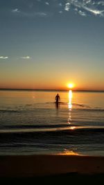 Silhouette of person wading in sea at sunset