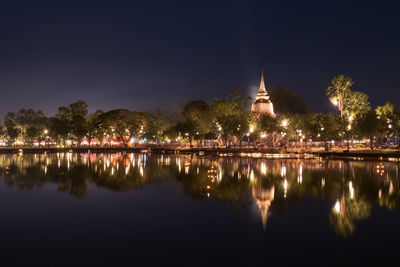 Illuminated building by lake against sky at night