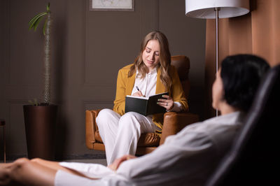 A female psychologist sits in a chair and listens to a client