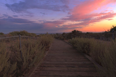 Boardwalk against cloudy sky during sunset