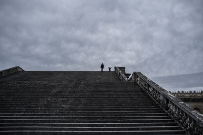 Low angle view of father and son moving down on staircase against cloudy sky