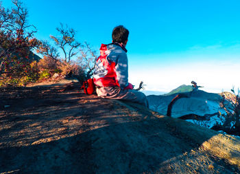 Young man sitting on mountain against clear sky