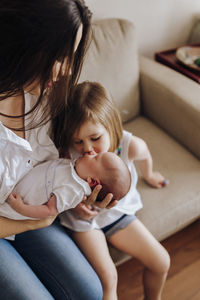 Older sister kissing newborn bother holding by mom. siblings and mother.