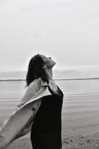 Rear view of woman standing at beach against sky