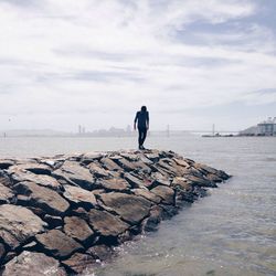 Man standing on rocks against cloudy sky