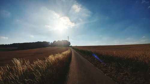 Empty road amidst agricultural field against sky