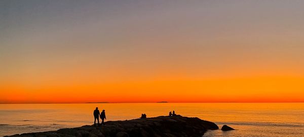 Silhouette people on beach against sky during sunset