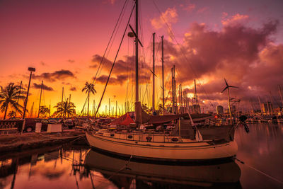 Sailboats moored on sea against cloudy sky during sunset