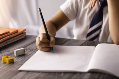 Selective focus on hand of an indian child writing with pencil on notebook wearing school uniform