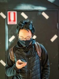 Portrait of young man using handphone against black and white patterned wall.