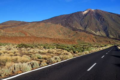 Empty road along rocky landscape against blue sky