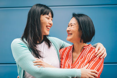 Smiling mother and daughter embracing against wall