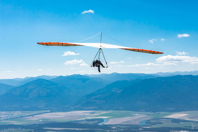 Low angle view of people paragliding over mountain against sky