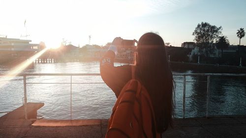 People photographing by river against sky during sunset