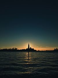 Silhouette of buildings by sea against sky during sunset