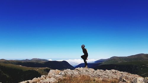 Side view of man standing on rock against blue sky